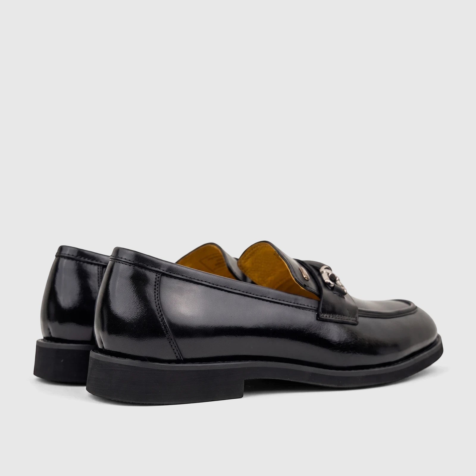 A pair of men's black leather dress slip-on shoes with metallic hardware detail, seen from a side-rear view.