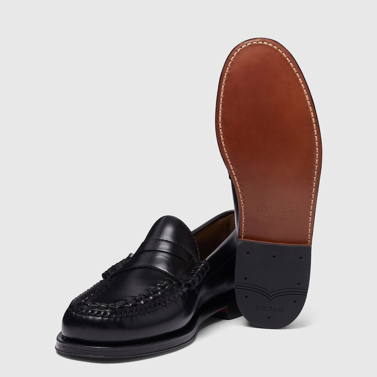 Black leather men's penny loafers with intricate woven vamp detail, showing one shoe lying flat and the other displaying its