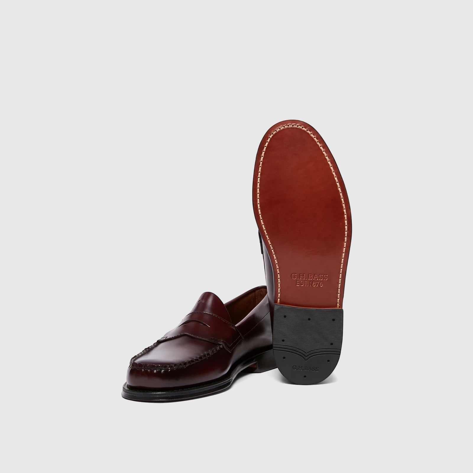 A pair of Bass Men's Weejun Logan Penny Loafers in wine leather, one presented standing to show the sole, the other lying on