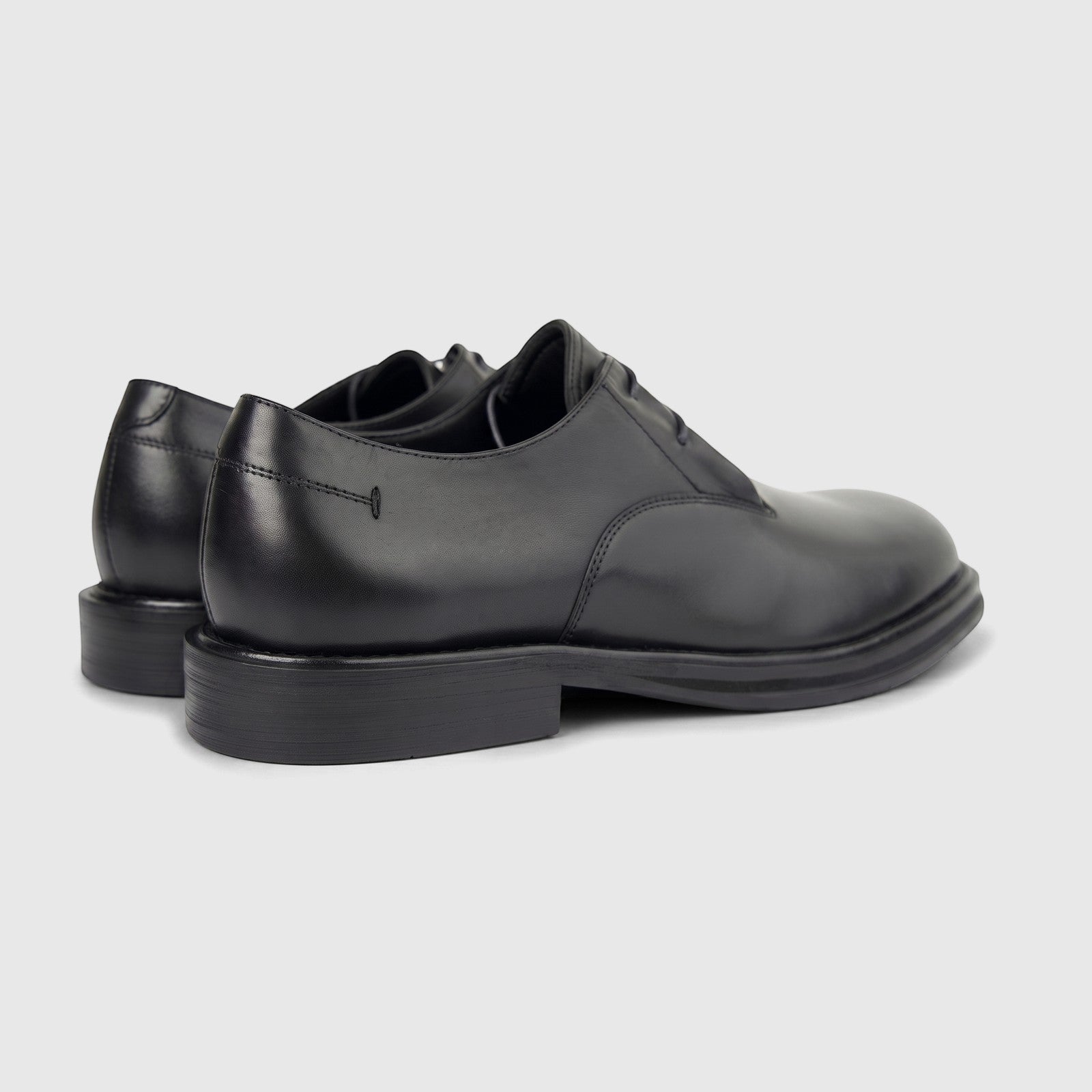 A pair of black leather formal derby shoes with chunky soles, shown from a side-rear perspective on a clean white background.
