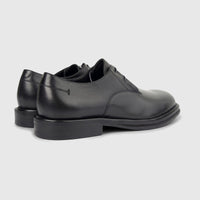 A pair of black leather formal derby shoes with chunky soles, shown from a side-rear perspective on a clean white background.