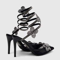 Bulbul Ladies' black high-heel evening sandals with rhinestone spiral ankle straps and flower embellishments, front view.