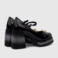 Black patent leather Mary Jane platform shoes with rhinestone-covered block heels and platforms, featuring gold bow accents.