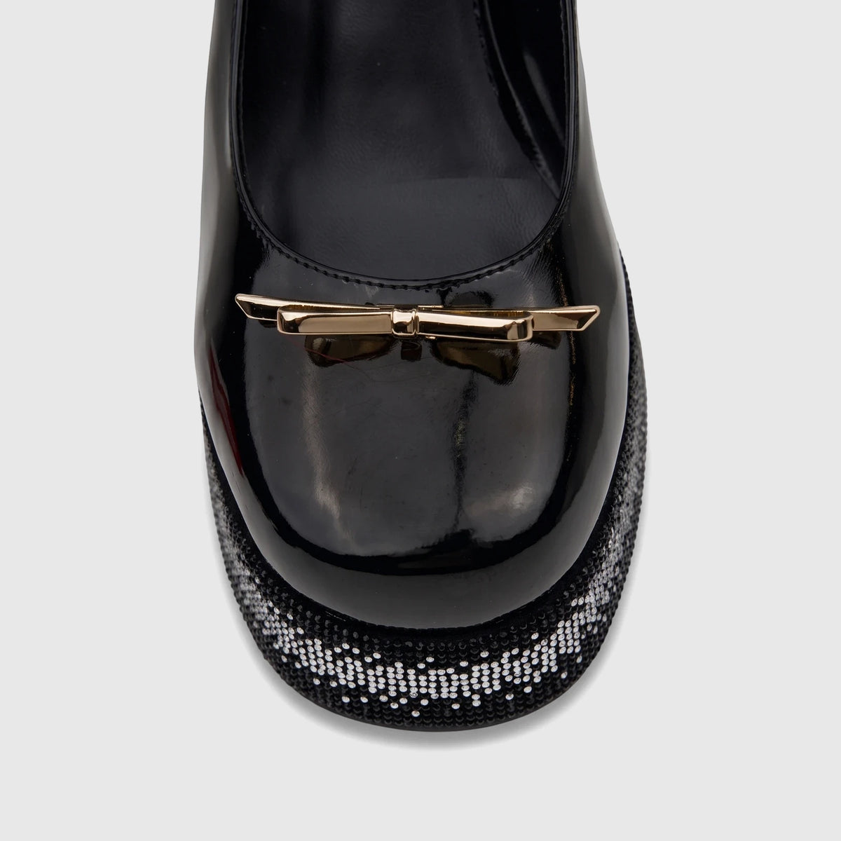 Close-up of a black patent leather Bulbul Ladies Block Heel Mary Jane shoe with a gold bow and bling platform.