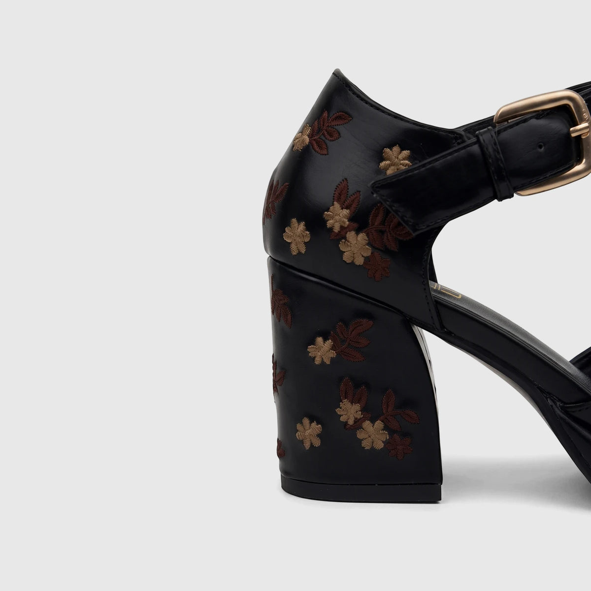 Close-up of a black leather Bulbul ladies block heel shoe with a T-bar strap, intricate floral embroidery, and a gold buckle.