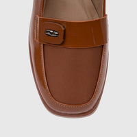 Close-up of a women's camel brown patent leather block heel sandal, featuring a decorative buckle and woven fabric detail.