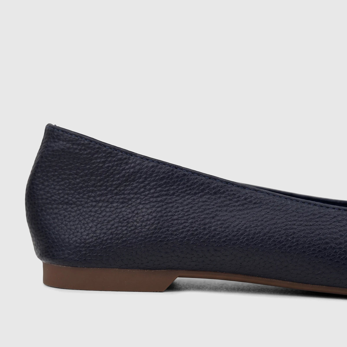 Side profile of a Bulbul Ladies Casual Pump in navy, featuring a pebbled texture and a flat brown sole.