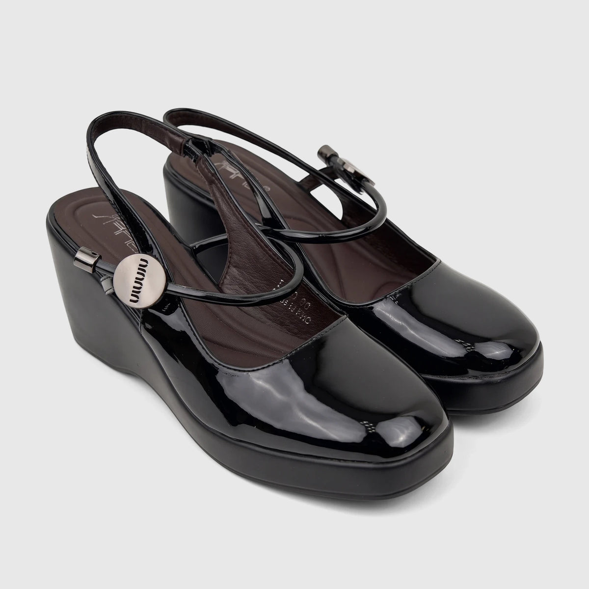 A pair of shiny black patent leather Bulbul Ladies Dress Block Heel Sandals with wedge heels and slingback straps on a white