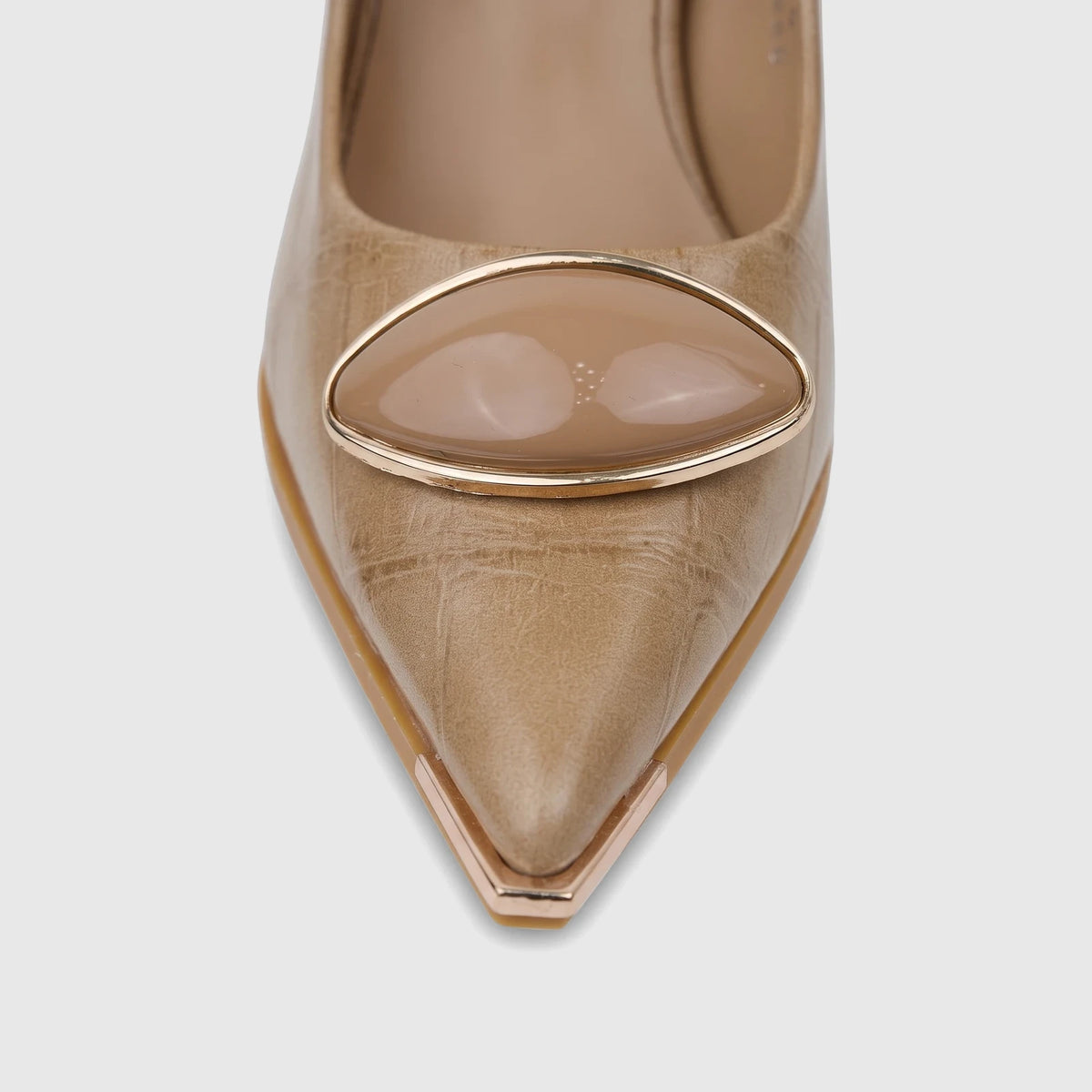 Close-up of a beige Bulbul ladies dress court shoe with a pointed toe and an oval metallic embellishment on a light