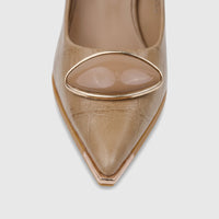 Close-up of a beige Bulbul ladies dress court shoe with a pointed toe and an oval metallic embellishment on a light