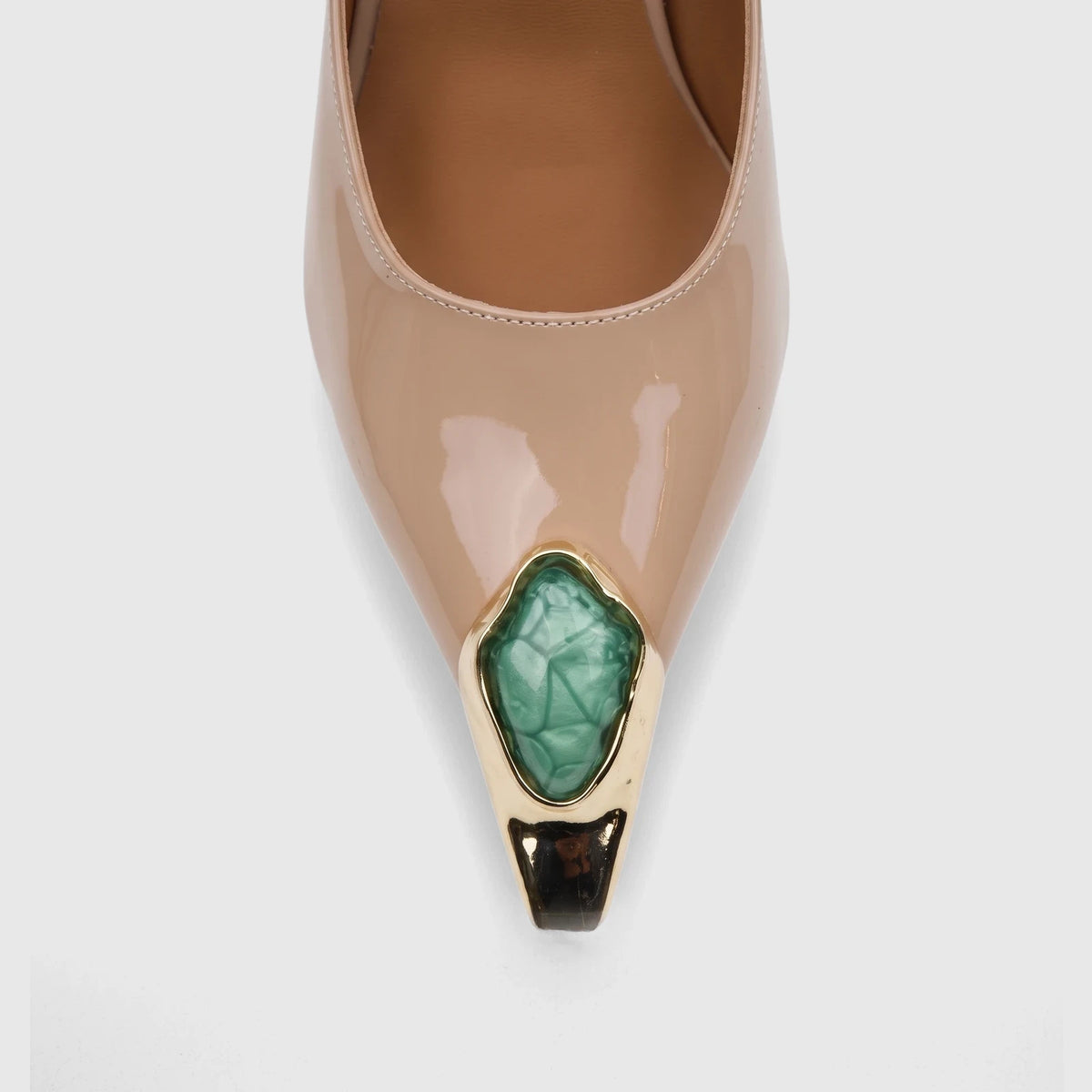 Close-up of a beige patent leather pointed-toe ladies' dress court shoe, featuring a green faceted stone set in gold at the