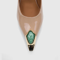 Close-up of a beige patent leather pointed-toe ladies' dress court shoe, featuring a green faceted stone set in gold at the