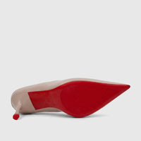 Nude patent leather stiletto court shoe with a pointed toe and red textured sole, viewed from the bottom.
