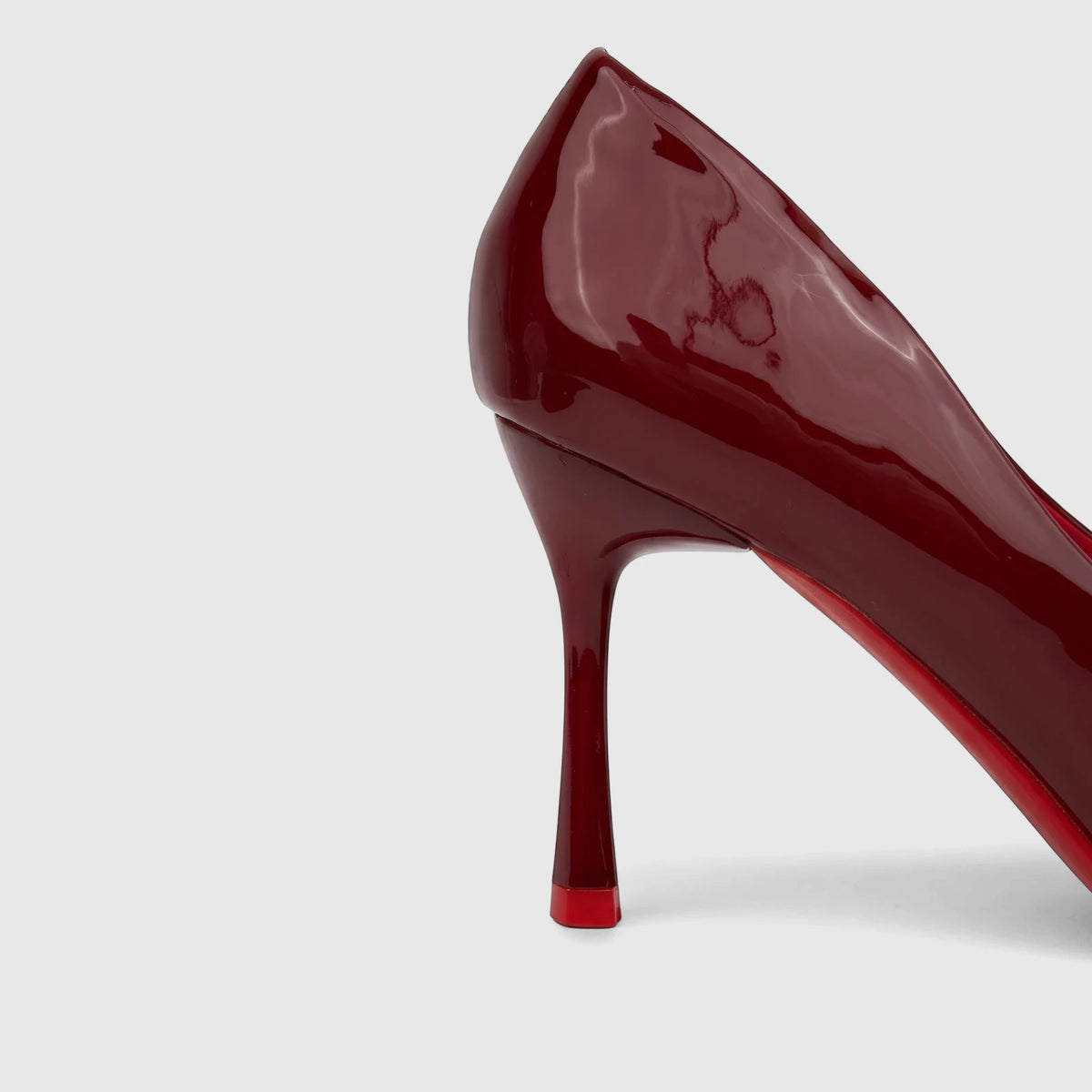 A side view of a glossy red patent leather Bulbul Ladies Dress Court Shoe, featuring a high heel and distinct red sole.