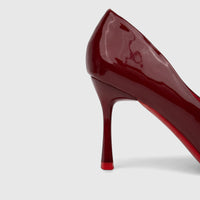 A side view of a glossy red patent leather Bulbul Ladies Dress Court Shoe, featuring a high heel and distinct red sole.