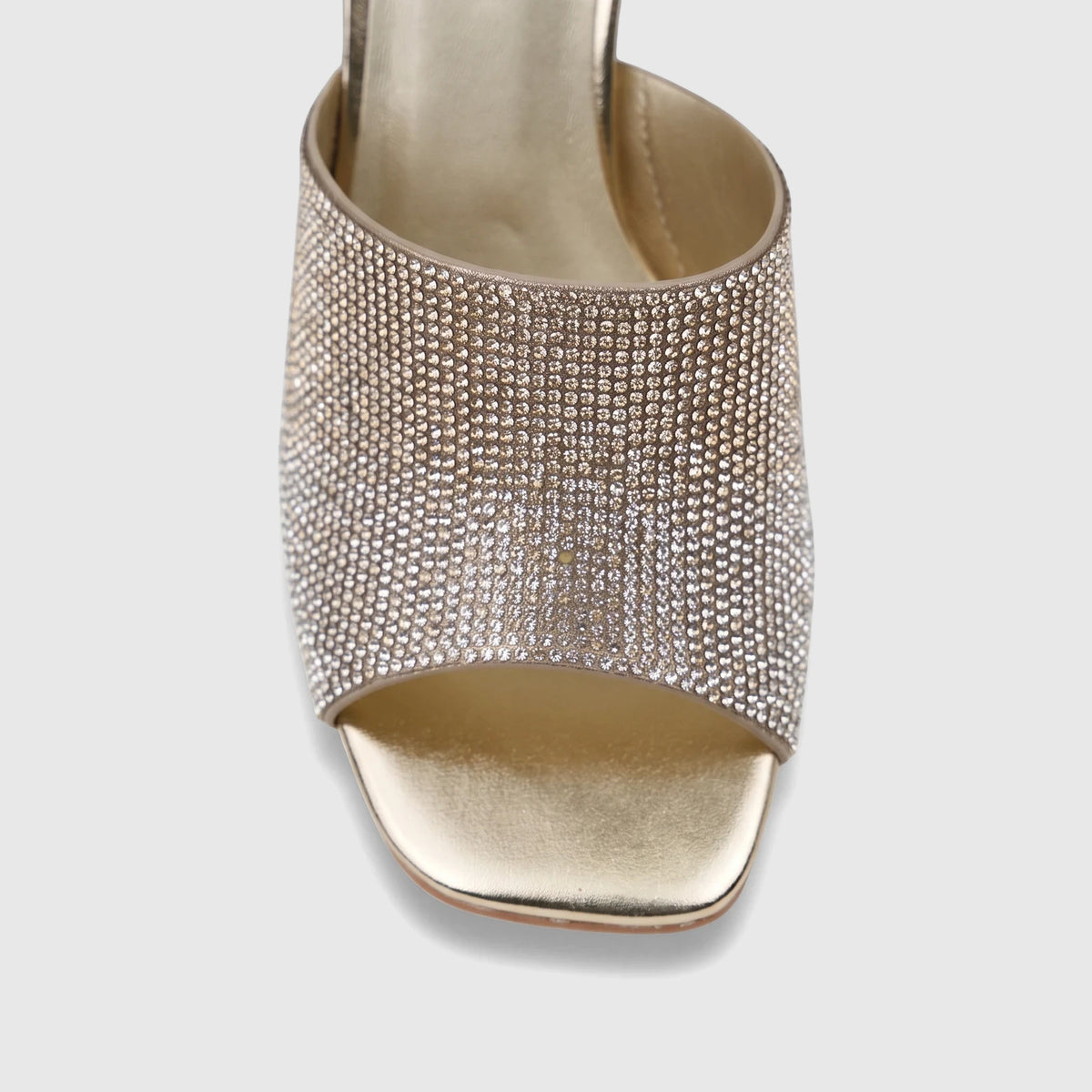 Close-up of a single gold ladies' evening block heel mule, heavily embellished with sparkling rhinestones, on a white