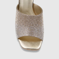 Close-up of a single gold ladies' evening block heel mule, heavily embellished with sparkling rhinestones, on a white