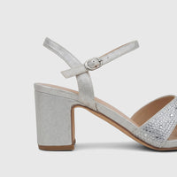 Close-up of a silver glitter block heel sandal with a rhinestone-embellished front strap and an adjustable ankle buckle.