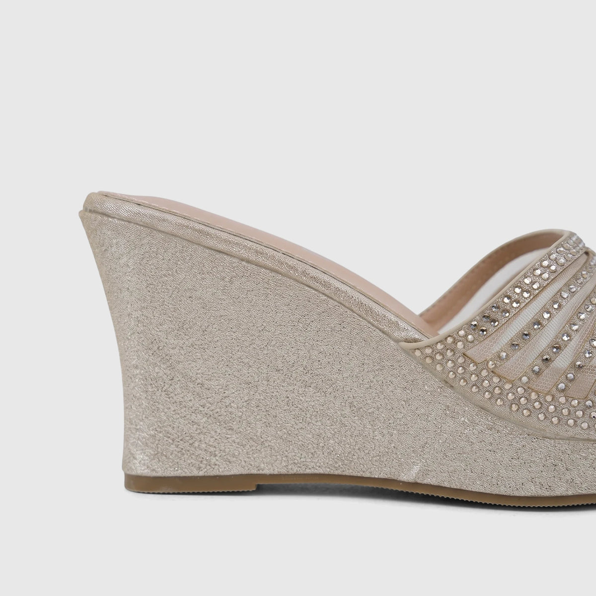 Close-up side view of a women's light gold wedge sandal with glitter detailing and rhinestone-embellished transparent mesh
