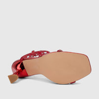 Red metallic high-heel sandal with spiral rhinestone straps, shown from a bottom-side view highlighting the textured sole