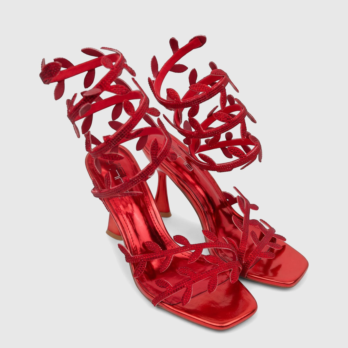A pair of shiny red Bulbul Ladies Spiral Strap Evening Heel Sandals with rhinestone-embellished leaf details, perfect for