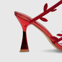 Close-up of a vibrant red metallic evening heel sandal featuring delicate spiral straps adorned with numerous sparkling