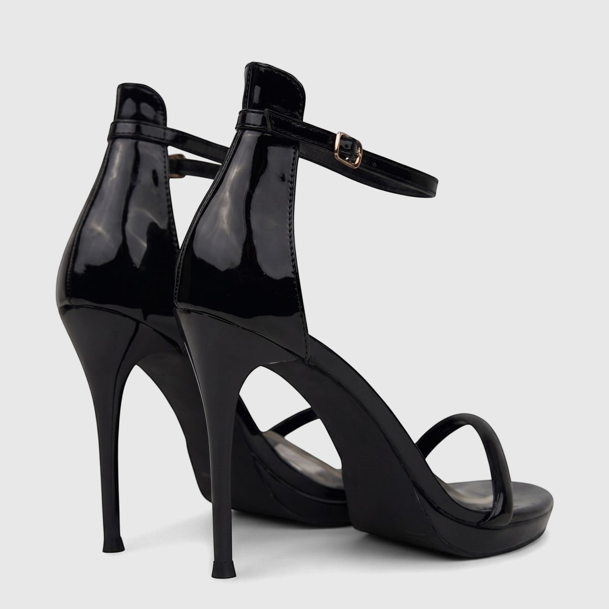 A pair of shiny black patent stiletto heel sandals with ankle straps and gold buckles, viewed from a back-three-quarter
