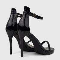 A pair of shiny black patent stiletto heel sandals with ankle straps and gold buckles, viewed from a back-three-quarter