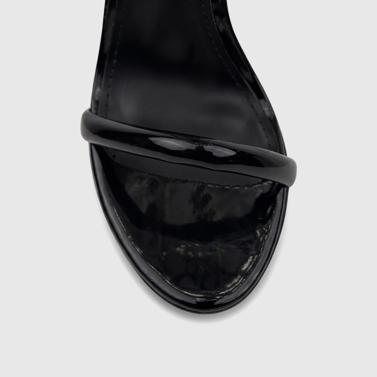 Close-up of a glossy black patent leather ladies stiletto heel sandal, showing the toe and forefoot strap.