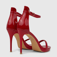 Red patent leather stiletto heel sandals for ladies, featuring an ankle strap and transparent toe strap, shown from a back