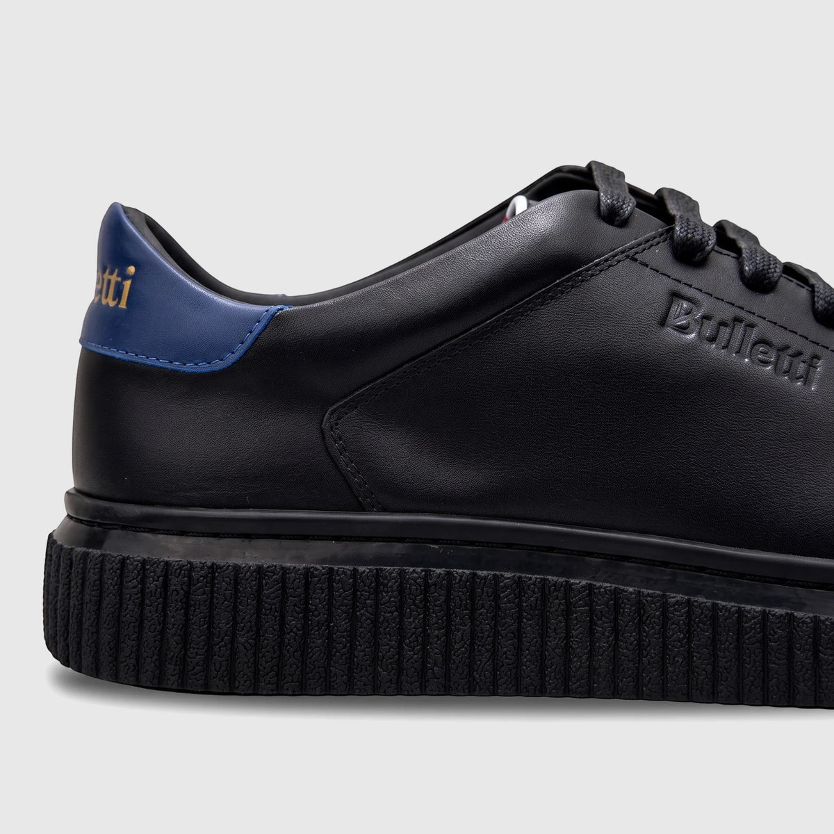 Bulletti Men's black leather sneakers with a blue heel accent and textured sole, shown from a side view.