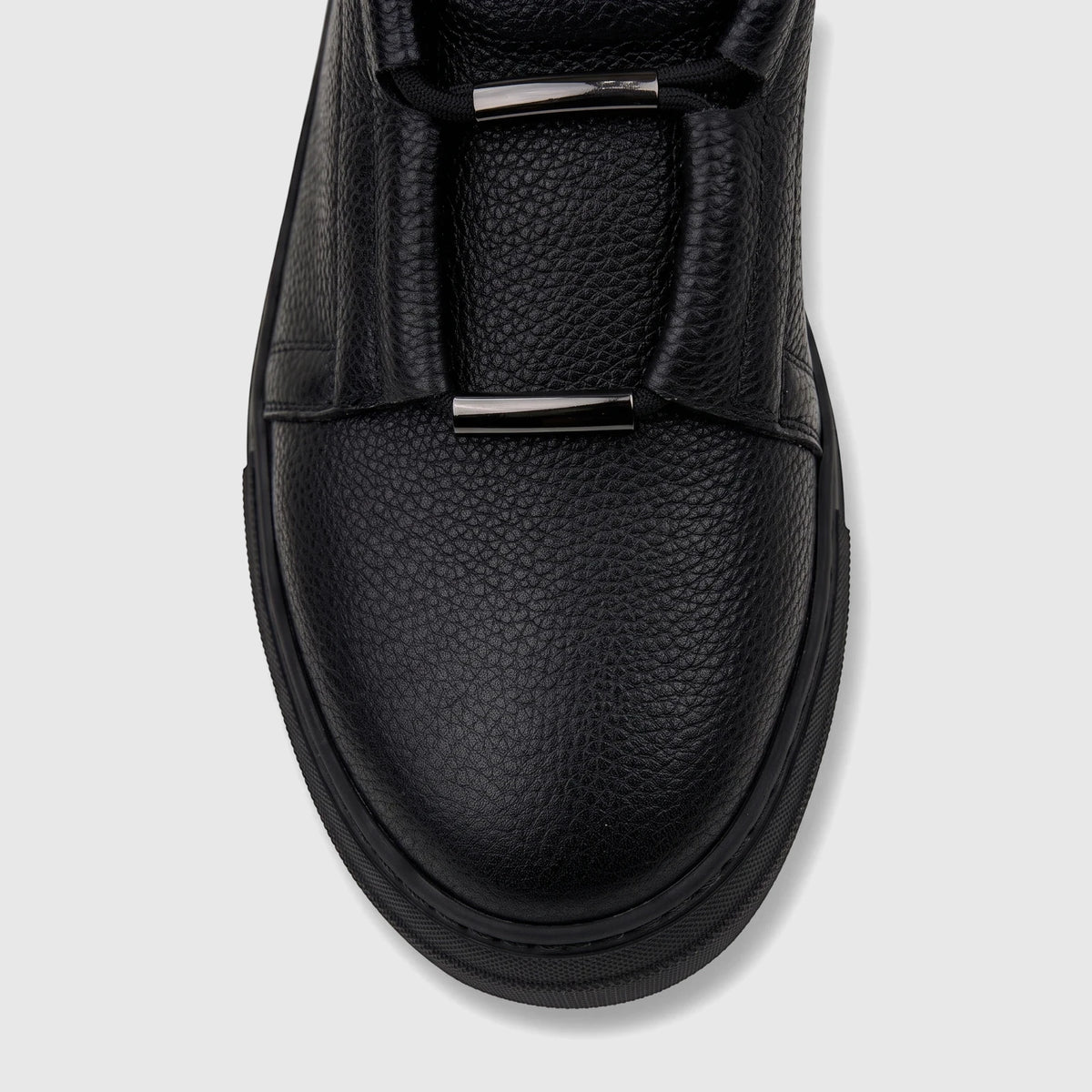 Close-up of a Bulletti Men's black leather sneaker, showing the pebbled texture, black laces, and metal bar accents.