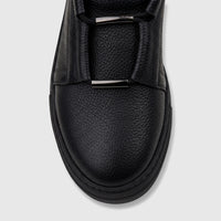 Close-up of a Bulletti Men's black leather sneaker, showing the pebbled texture, black laces, and metal bar accents.