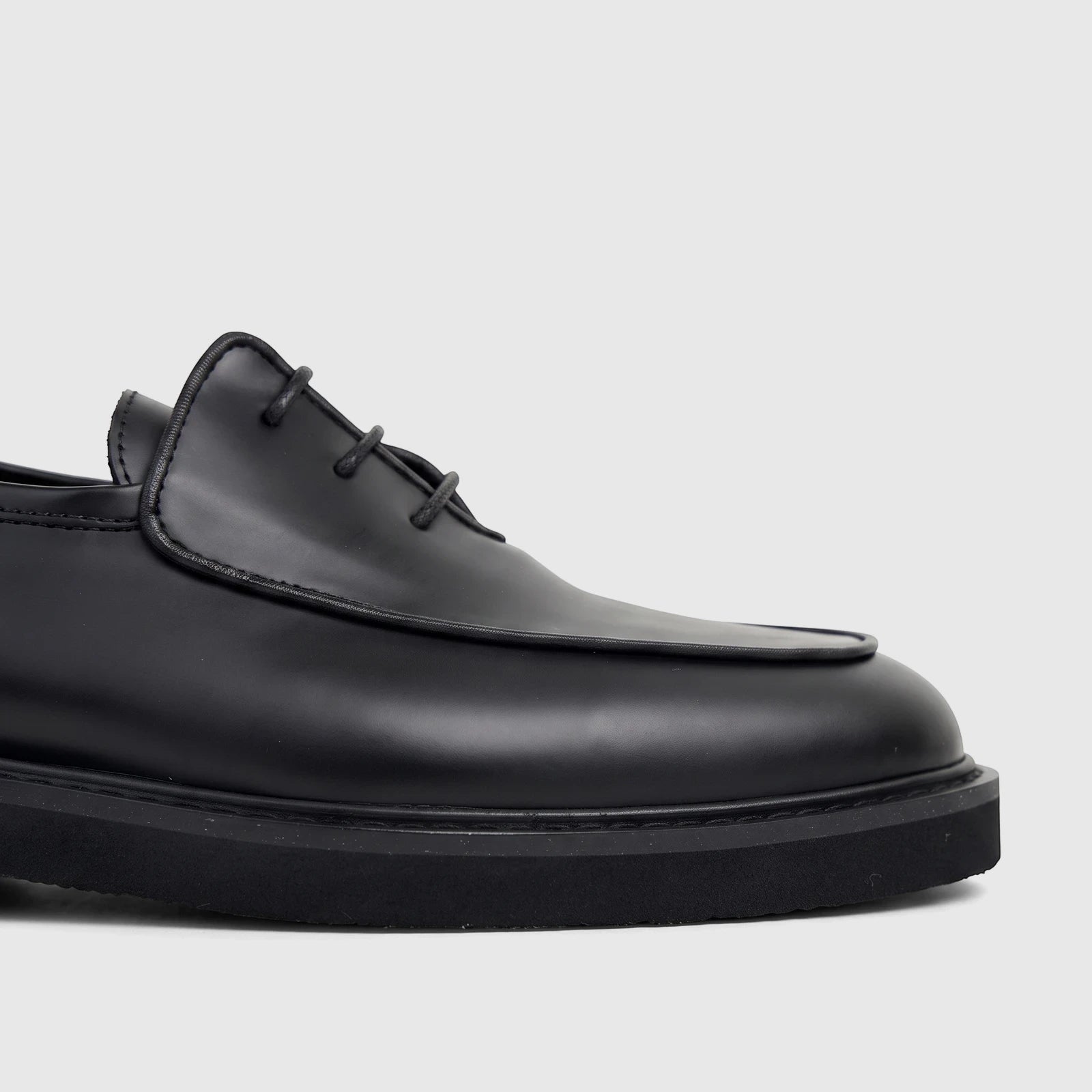 Close-up view of a Bulletti Men's black patent leather lace-up shoe with a chunky sole, showcasing its sleek design.