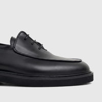 Close-up view of a Bulletti Men's black patent leather lace-up shoe with a chunky sole, showcasing its sleek design.