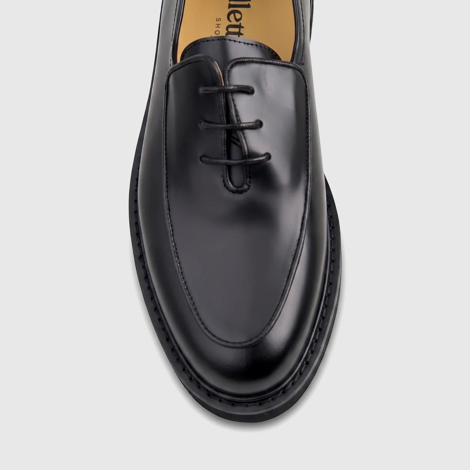 Close-up of a men's black patent leather lace-up shoe with a chunky sole, shown from a top-down perspective.