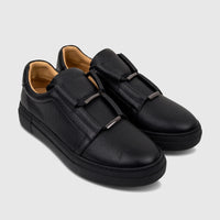 Bulletti men's black pebbled leather slip-on sneakers with metallic bar accents, angled view.