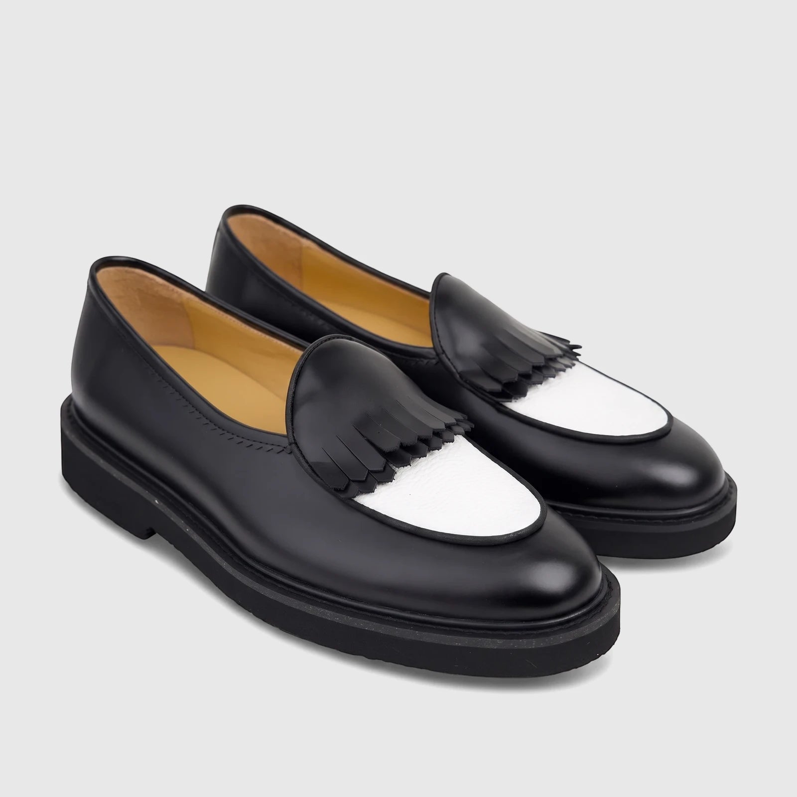 A pair of Bulletti men's black and white leather loafers with chunky soles and tassel fringe, angled view.