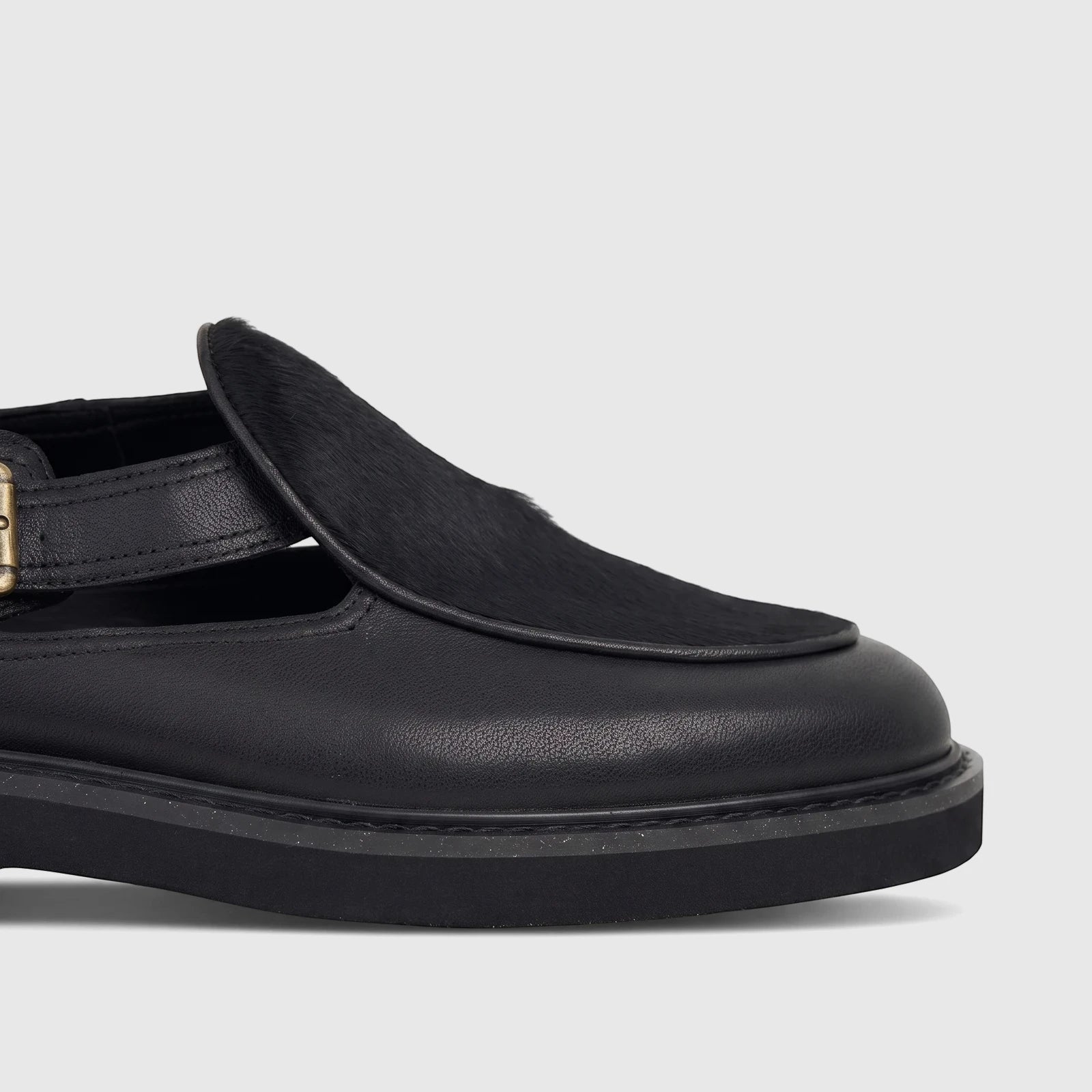 Close-up of a Bulletti Men's Leather Chunky Sole Sandal in black, featuring a strap with a brass buckle and a fur-like vamp