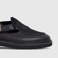 Close-up of a Bulletti Men's Leather Chunky Sole Sandal in black, featuring a strap with a brass buckle and a fur-like vamp