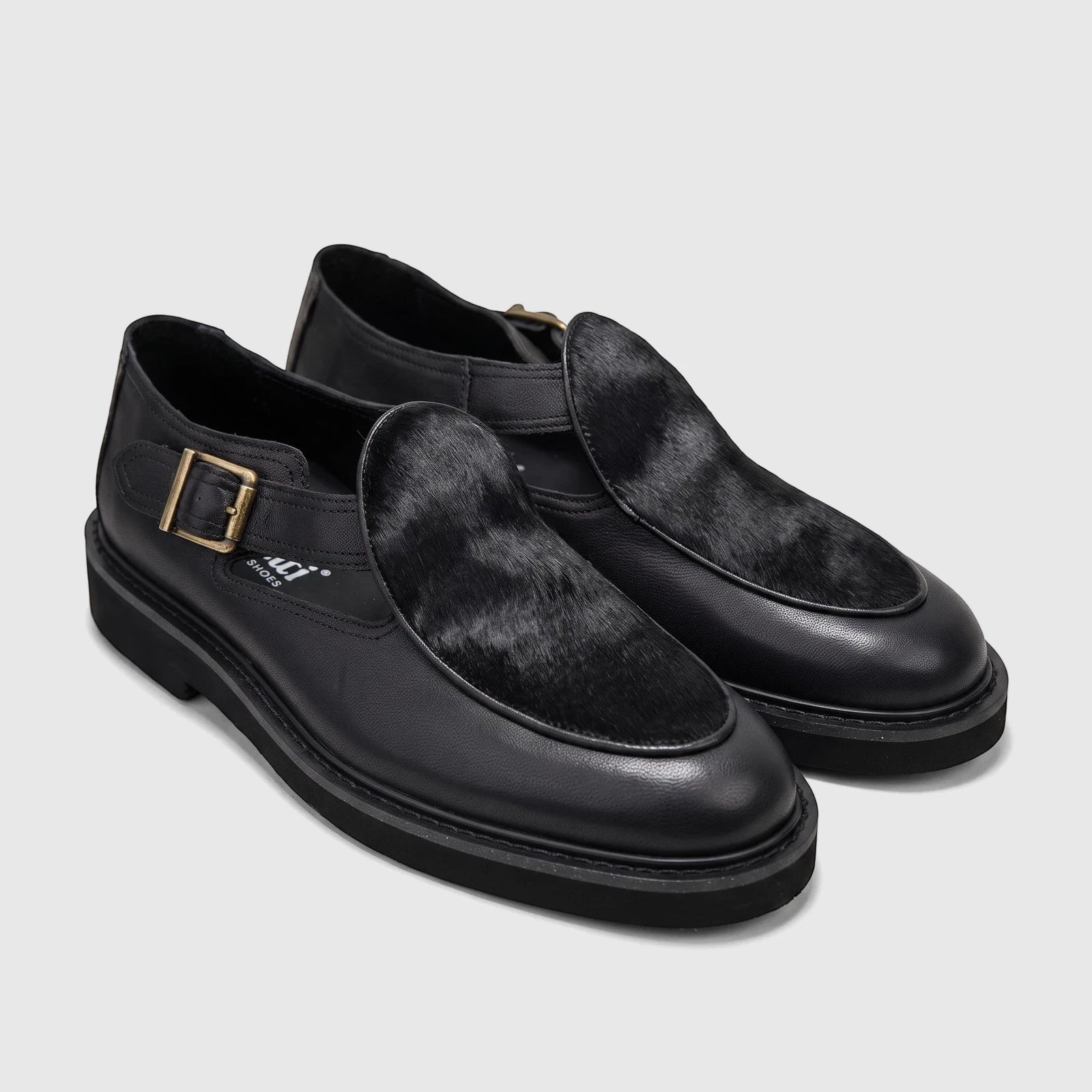 Pair of Bulletti Men's Leather Chunky Sole Sandals in black, featuring fur detail and a gold buckle closure, viewed from the