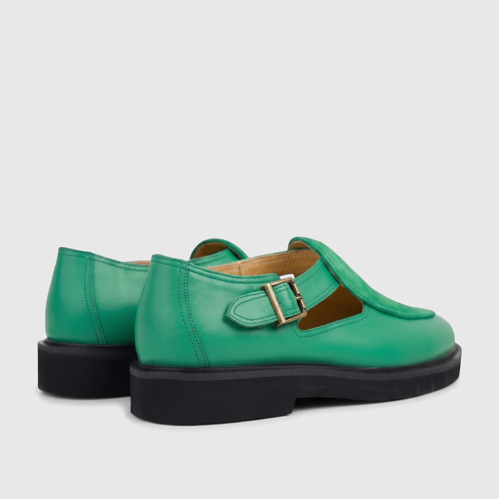 Pair of green leather unisex chunky sole sandals with brass buckles, viewed from a rear-side angle on a white background.