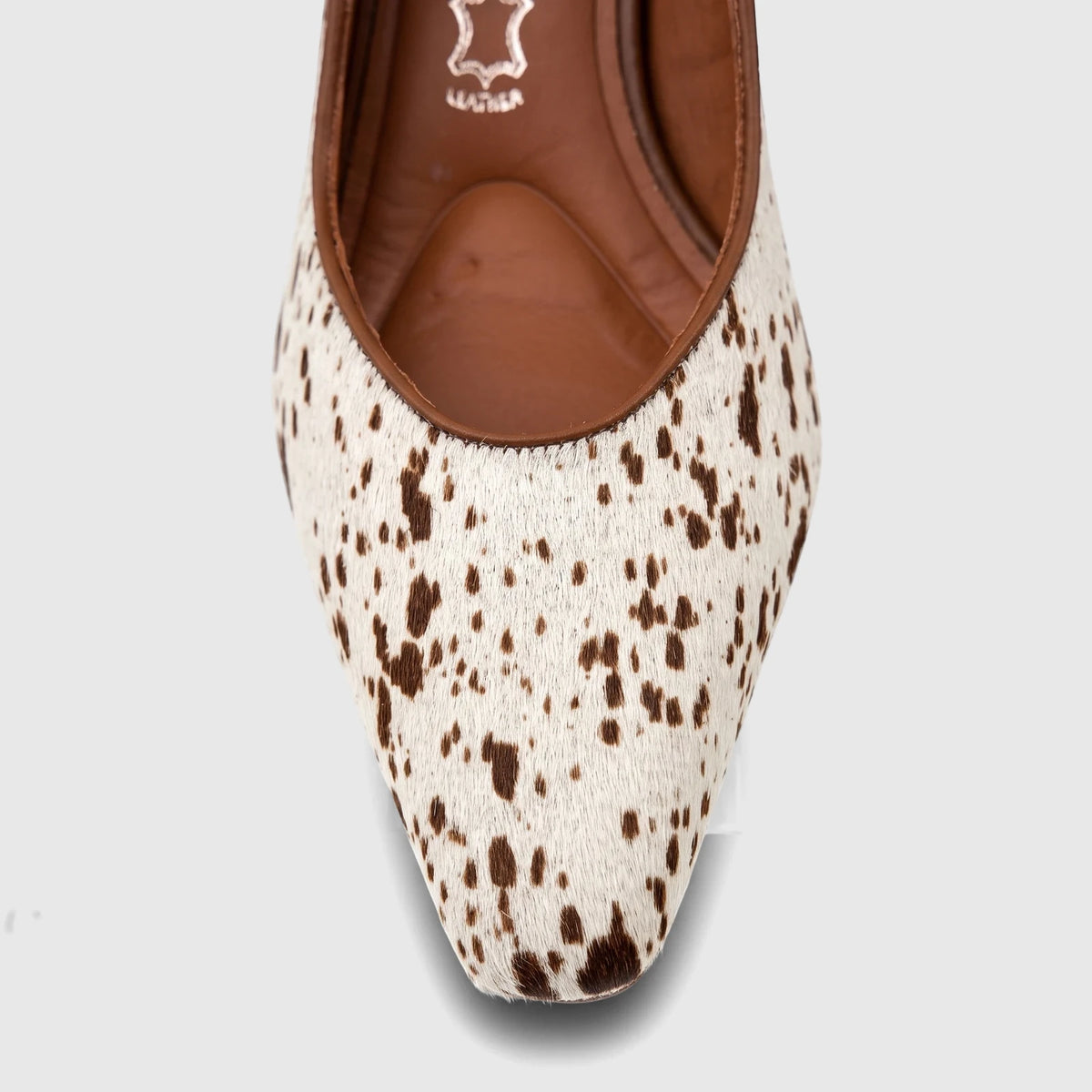 Close-up of a Capelli Rossi leather block heel court shoe in white and brown cow print, featuring a pointed toe.