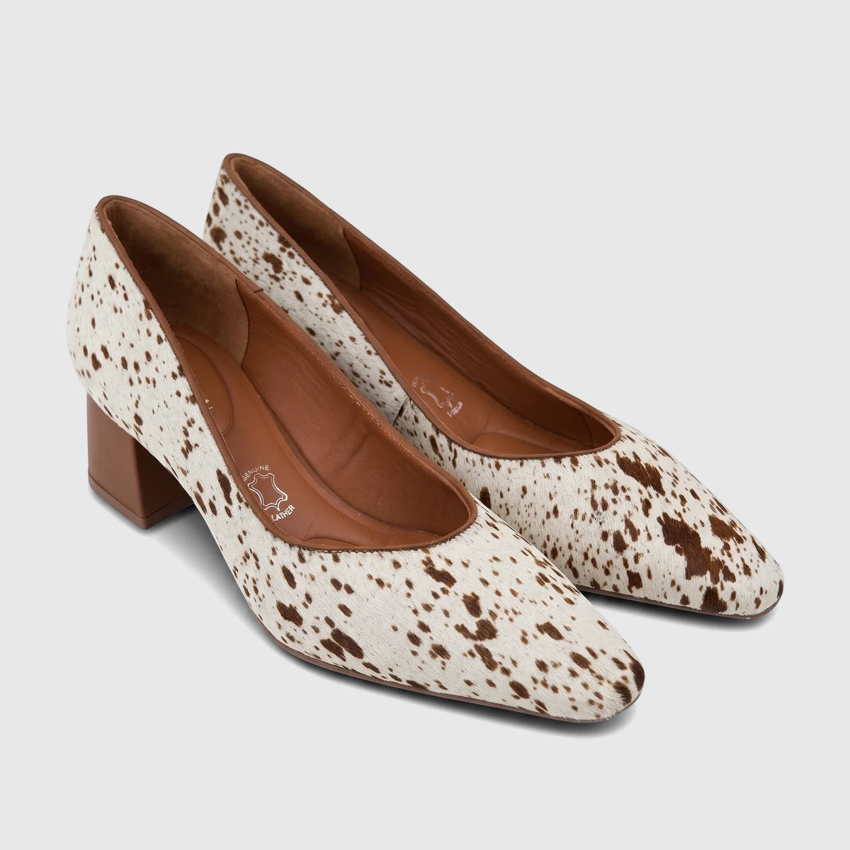 Pair of women's Capelli Rossi block heel court shoes in white and brown cow print leather, shown from an elevated side view.