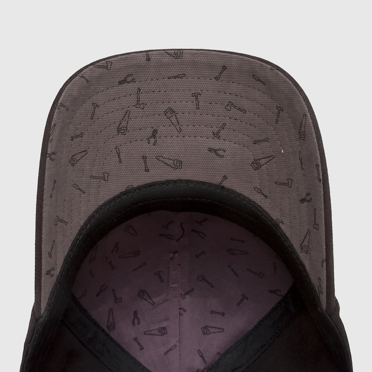 Underside view of a Cat Design Mark Aop Cap, black with a grey lining patterned with various hand tools.