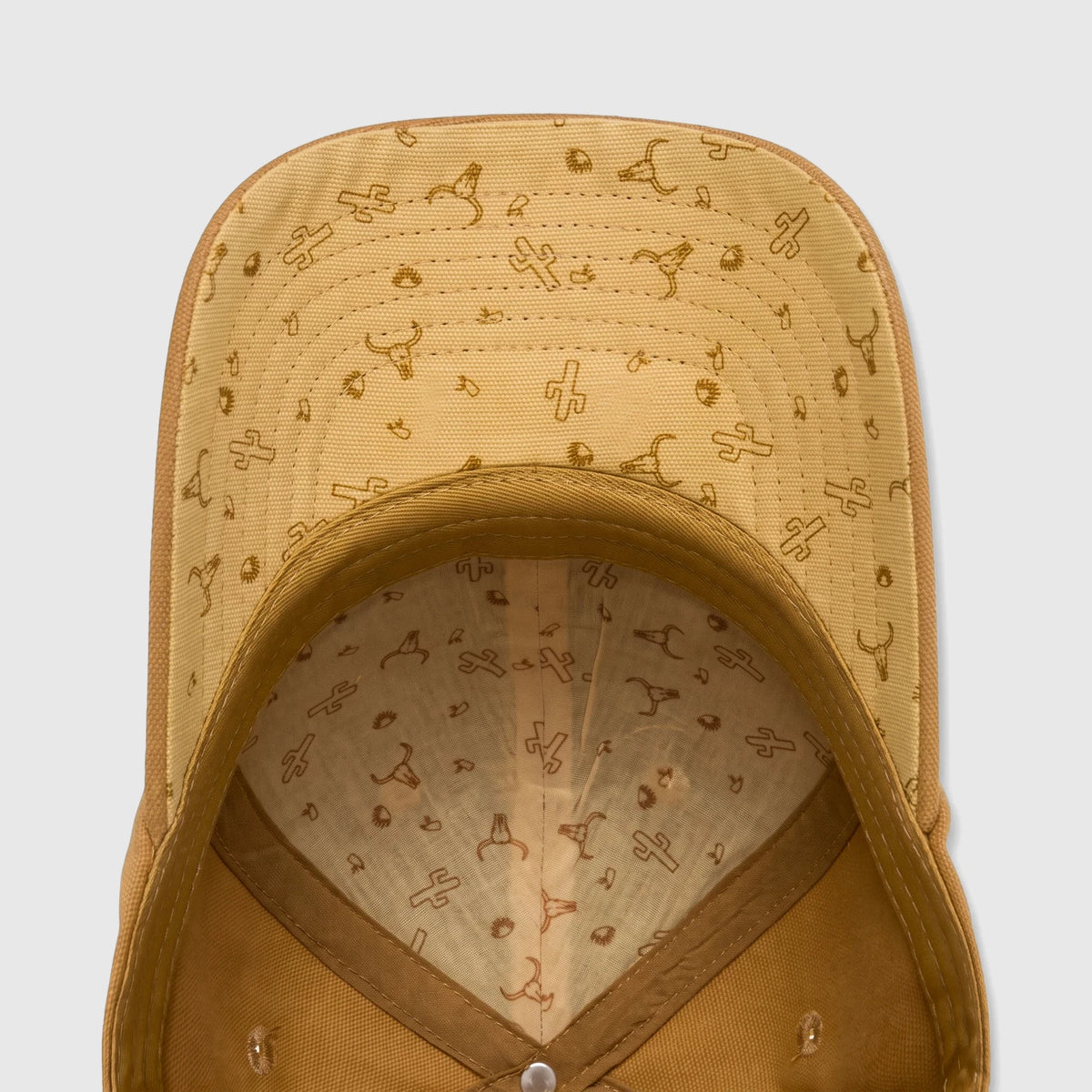 Bronze canvas baseball cap with a patterned underside featuring cactuses and bull skulls, shown from an overhead interior