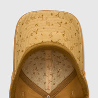 Bronze canvas baseball cap with a patterned underside featuring cactuses and bull skulls, shown from an overhead interior