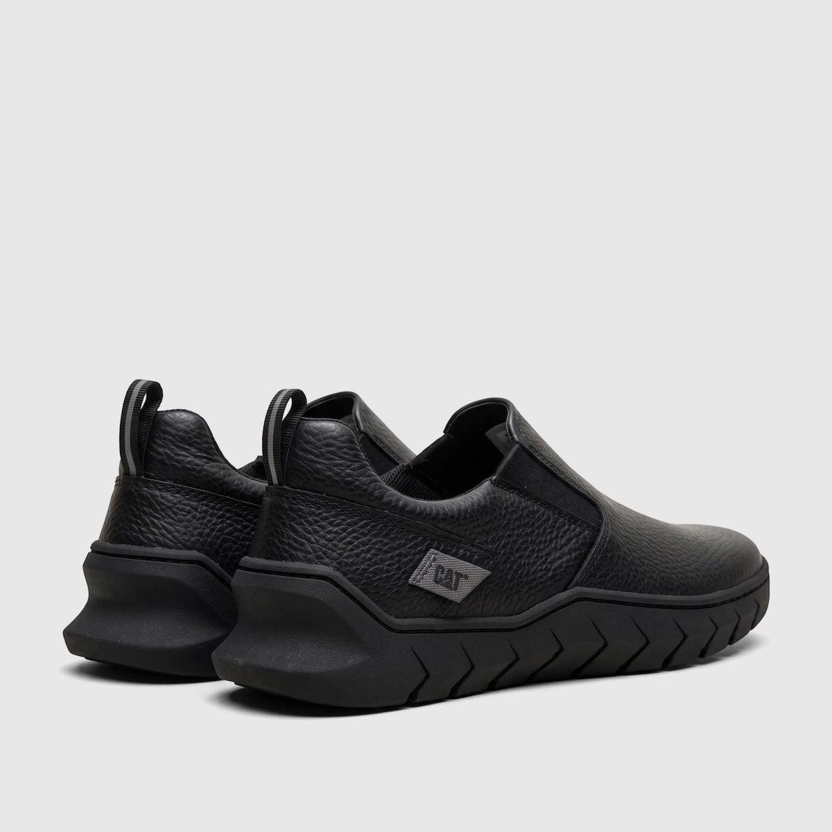 Pair of black Cat Men's Flexion slip-on shoes, seen from a rear three-quarter view, showcasing the textured upper and unique