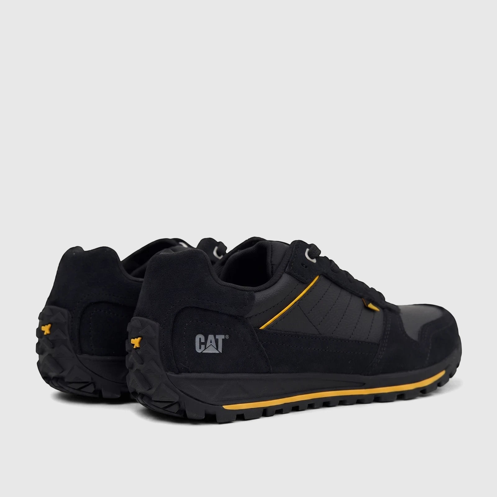 Pair of black Cat Men's Trigen P726923 CT401 sneakers with yellow accents, featuring a durable outsole, shown from a rear