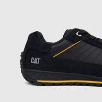 Side view of a black Cat Men's Trigen P726923 sneaker with yellow accents on the sole and side panels.
